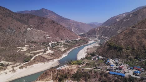 Aerial-view-of-winding-river-as-it-gracefully-carves-its-way-through-rugged-mountainous-terrain-with-small-remote-villages,-Countryside-Nepal