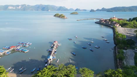 Aerial-view-of-Langkawi-pier,-Malaysia,-surrounded-by-boats,-water,-and-lush-green-hills-under-a-clear-sky