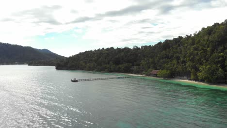 Picturesque-coastline-of-Kri-Island-in-Raja-Ampat,-Indonesia,-with-a-long-pier-extending-into-the-turquoise-waters