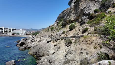 A-view-of-the-rocky-coastline-in-Sudak,-Crimea,-Russia,-with-buildings-in-the-distance