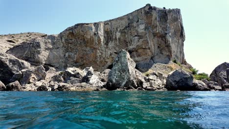 The-iconic-Sudak-Fortress-cliff-in-Crimea,-Russia,-viewed-from-the-water's-surface,-showcasing-the-towering-rock-formations-and-crystal-clear-waters