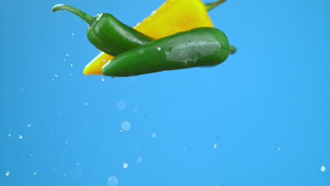 Green-and-yellow-chili-bell-peppers-jumping-in-air-with-water-droplets,-vegetables-for-cooking