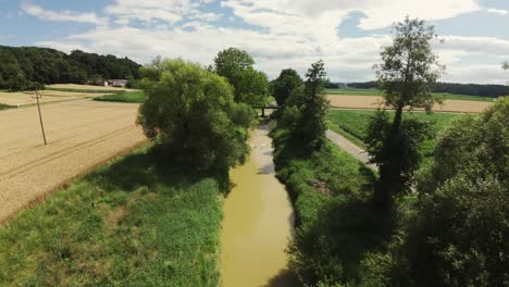 Eine-Drohne-Fliegt-über-Einen-Bach-Und-Einen-Bewässerungskanal-In-Einer-Ländlichen-Gegend-Mit-Feldern-Und-Bäumen