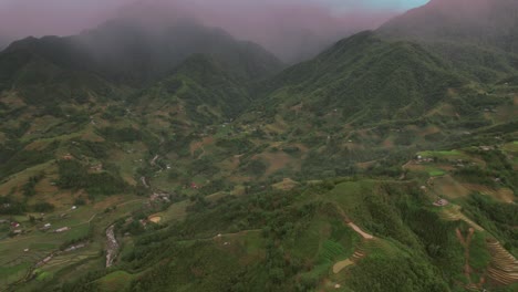 Journey-of-the-drone-from-the-top-of-the-foggy-mountains,-going-down-through-hill,-villages-and-water-streams,-ending-in-a-rice-field