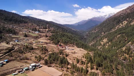 Farming-Land-surrounded-by-Forest-and-Mountainous-Landscape-in-Nepal-Annapurna-Trek-with-Himalaya-Snow-Capped-Mountains,-Remote-Nepal-Aerial-Drone-Shot