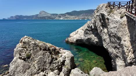 A-view-of-the-coastline-at-Sudak,-Crimea,-Russia,-featuring-clear-blue-water,-rocky-cliffs,-and-a-small-cove