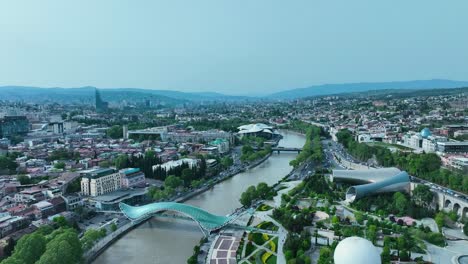 Drohnenaufnahmen-Für-Die-Friedensbrücke-In-Georgien,-Tiflis,-Mit-Wunderschöner-Landschaft-Der-Ganzen-Stadt-Bei-Klarem-Himmel-Und-Sonnigem-Wetter