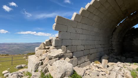 hermitage-of-San-Pedro,-14th-century,-with-a-turn-of-the-camera-we-see-many-stones-on-the-ground,-we-appreciate-its-spectacular-vaults-with-rectangular-blocks-of-granite-we-see-a-blue-sky-with-clouds