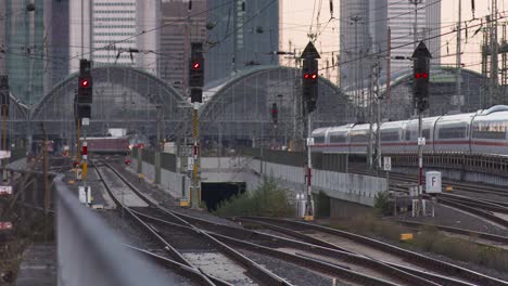 Eisenbahnschienen,-Die-In-Der-Abenddämmerung-In-Einen-Stadtbahnhof-Führen,-Mit-Mehreren-Signalen-Und-Einem-Abfahrenden-Zug