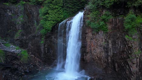 Toma-Panorámica-De-Una-Cascada-Que-Fluye-Desde-El-Lado-Del-Acantilado-En-Un-Bosque-Siempre-Verde-En-El-Noroeste-Del-Pacífico.