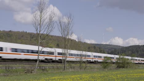 Hochgeschwindigkeitszug-Rast-Durch-Eine-Malerische-Landschaft,-Windturbinen-Im-Hintergrund