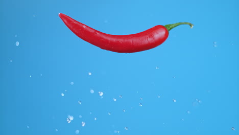 Un-Solo-Pimiento-Rojo-Picante-Volando-Hacia-Arriba,-Saltando-Y-Permaneciendo-Horizontal,-Con-Gotas-De-Agua