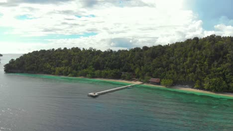 Aerial-orbit-shot-of-the-lush,-forested-hills-and-turquoise-waters-of-Kri-Island-in-Raja-Ampat,-Indonesia,-with-a-long-pier-extending-into-the-sea