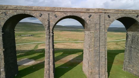 Flying-through-tall-stone-arches-of-viaduct-railway-bridge-spanning-moorland-at-golden-hour