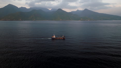 Barco-Marítimo-Navega-A-Través-Del-Océano-Frente-A-La-Costa-Montañosa-De-Bali,-Aéreo