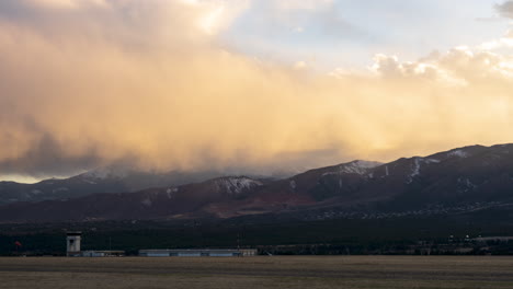 Rain-falls-in-the-mountains-of-Colorado-as-the-sun-sets,-casting-beautiful-oranges,-pinks,-and-reds-onto-the-falling-rain