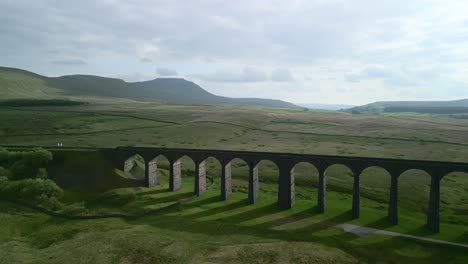 Arched-railway-viaduct-bridge-crossing-moorland-with-flat-topped-mountain-on-horizon-and-long-shadows-at-golden-hour