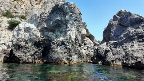 Clear,-calm-water-surrounds-large-rock-formations-at-Sudak-Bay-in-Crimea,-Russia