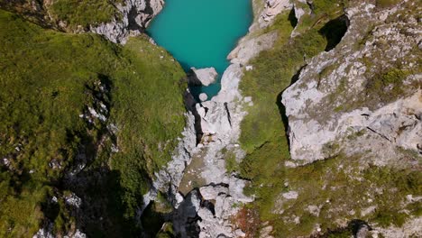 Aerial-view-of-a-turquoise-lake-surrounded-by-rugged-rocky-terrain-and-lush-green-vegetation