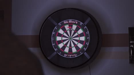 Person-throwing-darts-at-a-dartboard,-hitting-triple-20-three-times,-in-a-dimly-lit-room