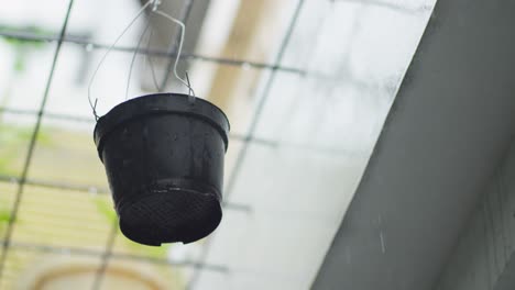 Black-bucket-hanging-in-the-rain-under-a-metal-grid-roof-on-a-rainy-day