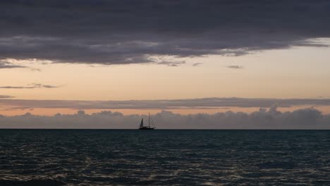 Surreal-blue-hour-ocean-waves,-lone-sailing-yacht-on-dark-horizon