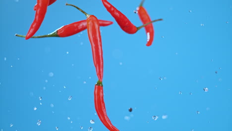 Una-Explosión-De-Chiles-Rojos-Volando-En-El-Aire-Con-Gotas-De-Agua