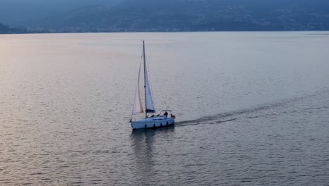 Cálido-Resplandor-En-El-Agua-Del-Lago-Y-Velero-Navegando-Por-El-Encantador-Lago-Maggiore-En-Italia.