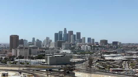 Aerial-view-of-train-tracks-along-Los-Angeles-river,-downtown-skyline-in-the-distance