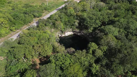 Low-flyover-tilts-down-to-reveal-Cenote-Kikil-in-north-Yucatan,-Mexico