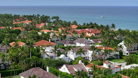 Aerial-view-of-a-luxurious-coastal-neighborhood-with-red-tiled-roofs,-lush-palm-trees,-and-a-serene-ocean-backdrop