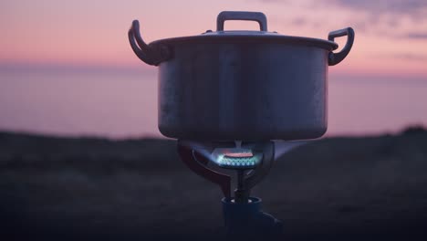 Kochendes-Wasser-Mit-Einem-Gaskocher-Draußen-In-Der-Nähe-Einer-Klippe-Mit-Dem-Sonnenuntergang-Dahinter