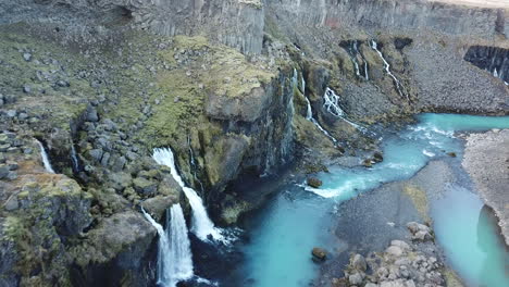 Highlands-of-Iceland,-Drone-Aerial-View-of-Waterfall-From-Volcanic-Cliffs-and-Glacial-River-Canyon