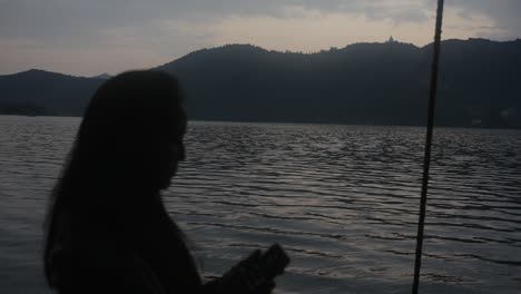 Silhouette-Eines-Mädchens,-Das-Telefoniert-Und-Während-Der-Dämmerung-Das-Wunderschöne-Meer-Und-Die-Berge-In-Nepal-Genießt---Nahaufnahme