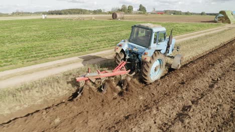 Ein-Traktor-Pflügt-An-Einem-Sonnigen-Tag-Das-Feld-Zum-Pflanzen-Von-Saatgut-Auf-Einem-Landwirtschaftlichen-Bauernhof-In-Lettland---Luftaufnahme