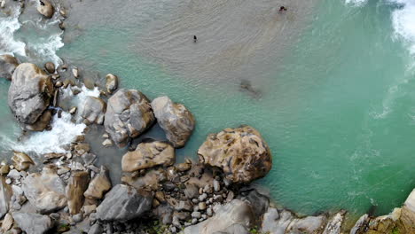 Aerial-river-bank-with-big-rocks-alongside-a-huge-waterfall