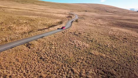 Toma-De-Drone-De-Un-Automóvil-Conduciendo-Por-Una-Carretera-En-Un-Parque-Nacional-Al-Sur-De-Las-Tierras-Altas-De-Escocia.