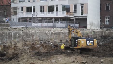 Ein-Gelber-Cat-Bagger-Gräbt-In-Zeitlupe-Ein-Loch-Auf-Einer-Baustelle