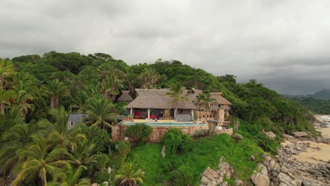 Aerial-View-of-Buildings-With-Thatched-Roof-Surrounded-by-Tropical-Landscape-in-Sayulita-Beach-on-a-Cloudy-Day