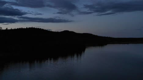 4K-drone-footage-flying-over-dark-waters-at-dusk-toward-lakeshore-with-purple-sky-in-background