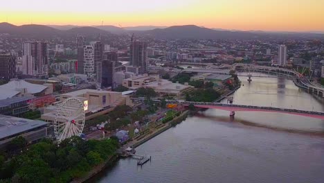 Aerial-view-of-Brisbane-city-South-bank-with-a-Ferris-wheel,-bridge,-river-and-buildings-at-sunset