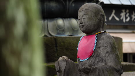 Cinematic-revealing-of-a-Buddha-statue-wearing-a-red-bib-in-Senso-ji-temple,-Tokyo