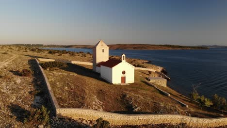 Rural-Church-on-a-tiny-island-in-sunset-near-Zadar,-Croatia,-circling-with-drone