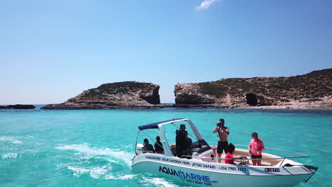 Drone-flying-by-a-small-boat-in-slow-motion-driving-along-the-blue-lagoon-on-comino-island-in-malta