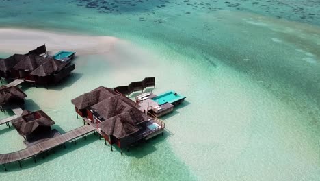 Aerial,-reverse,-drone-shot,-of-a-couple,-sitting-in-a-pool,-at-a-villa,-in-swallow,-turquoise-sea,-on-a-sunny-day,-on-the-Conrad-Rangali-island,-in-Maldives