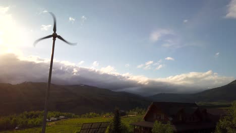 A-wind-turbine-is-seen-spinning-near-a-cabin-with-a-green-meadow-in-the-background