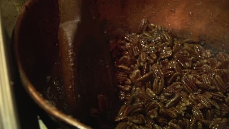 Close-up-slow-motion-shot-of-roasted-caramelised-pecan-nuts-being-stirred-with-a-big-wooden-paddle