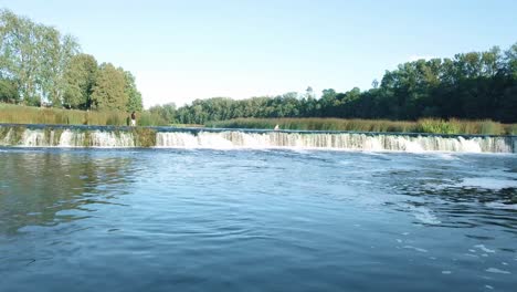 Hyperlapse-from-drone-flying-low-over-flowing-river-toward-wide-short-waterfall