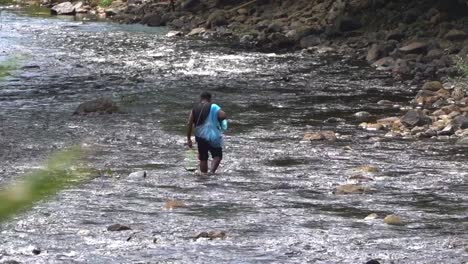 Un-Hombre-Tailandés-Camina-A-Lo-Largo-De-La-Orilla-Rocosa-De-Un-Río-Con-Su-Captura-En-Cámara-Lenta