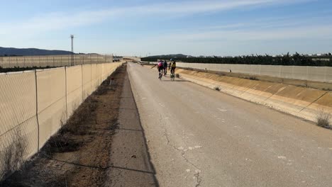 Cyclists-in-cyclist-clothing-taking-daily-exercise-along-road-running-next-to-aqueduct-in-Spain,-in-slow-motion